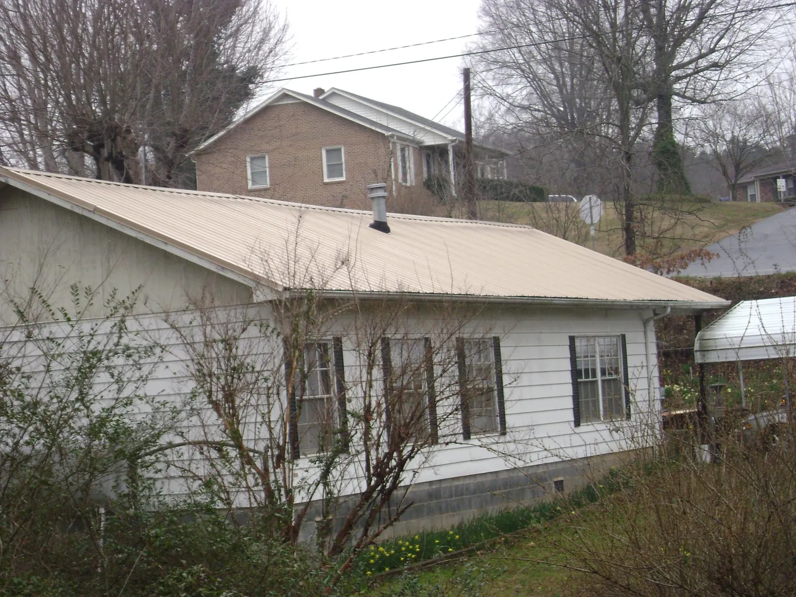 Tan metal roof on a white sided house set into a hillside — Commercial Roofing by Roofing Brothers in Melville