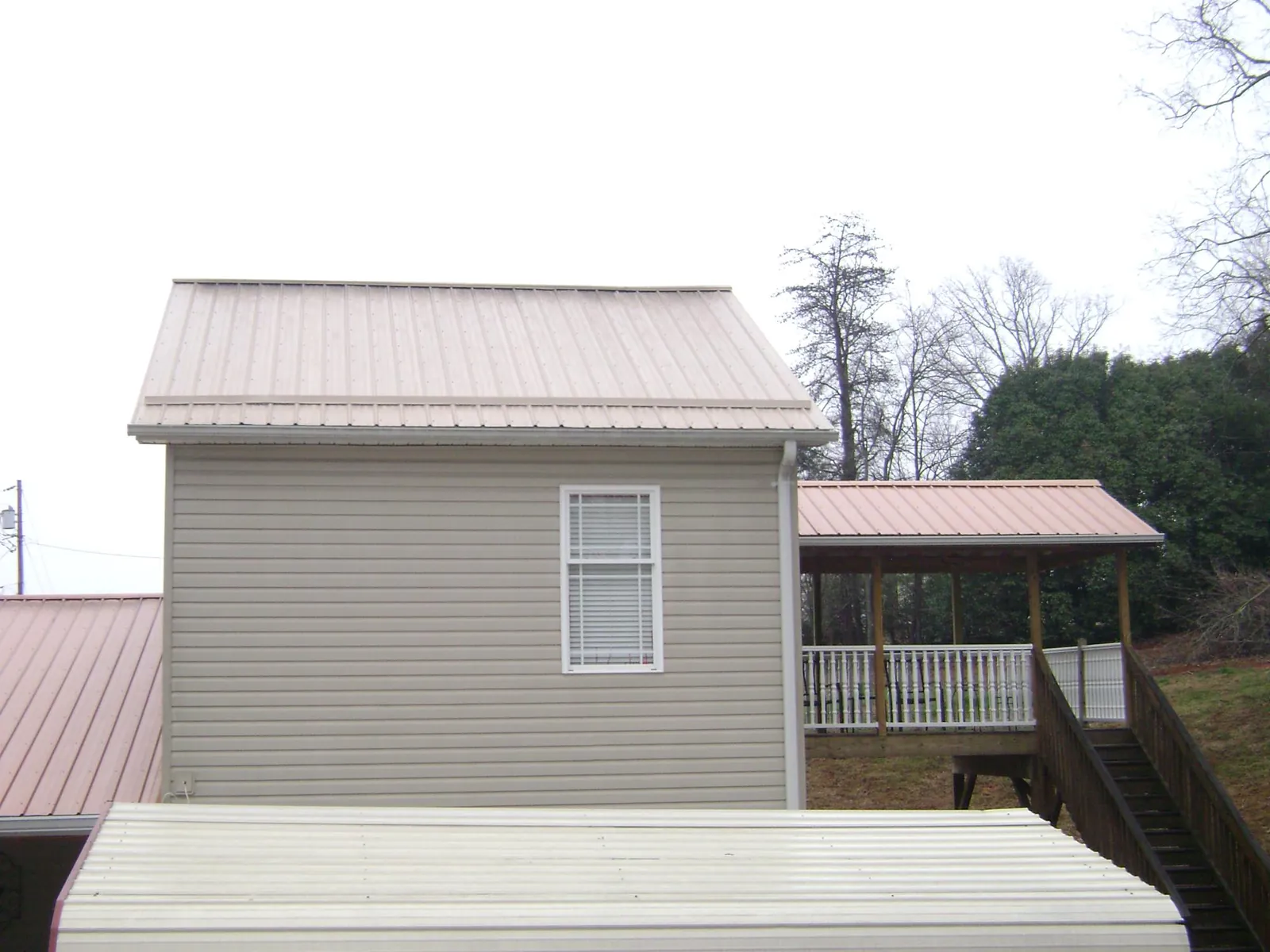 Tan metal roofs on a two story addition and attached porch, from a Roof Replacement job in Melville